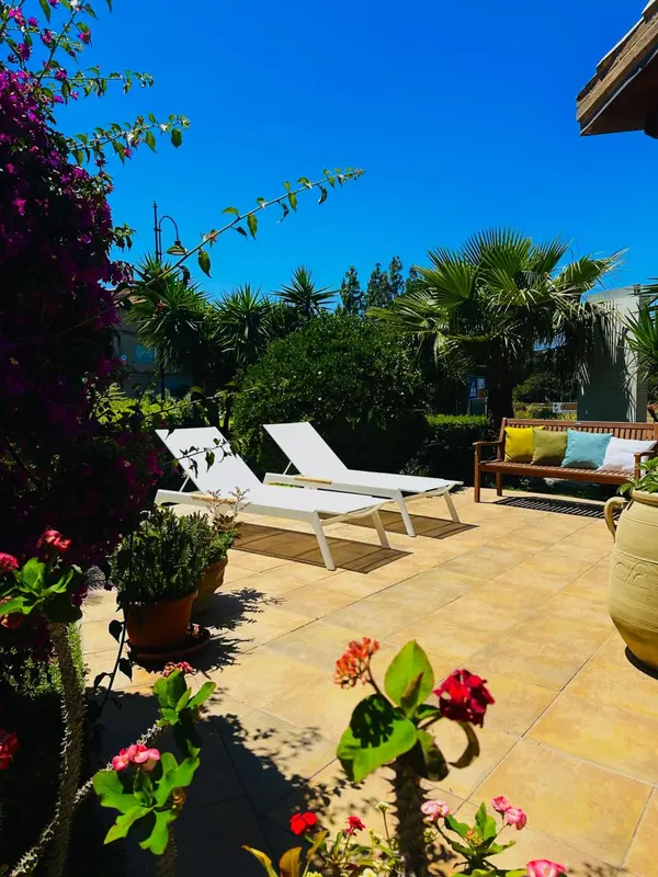 Deux transats blancs sur une terrasse ensoleillée, entourée de végétation luxuriante.