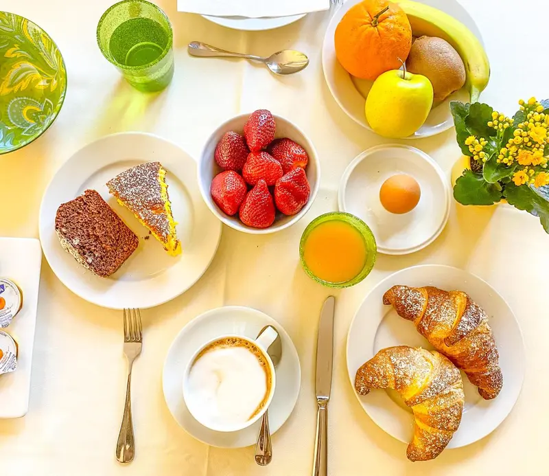 Une table est dressée avec un petit-déjeuner composé de fruits, de viennoiseries et de boissons.