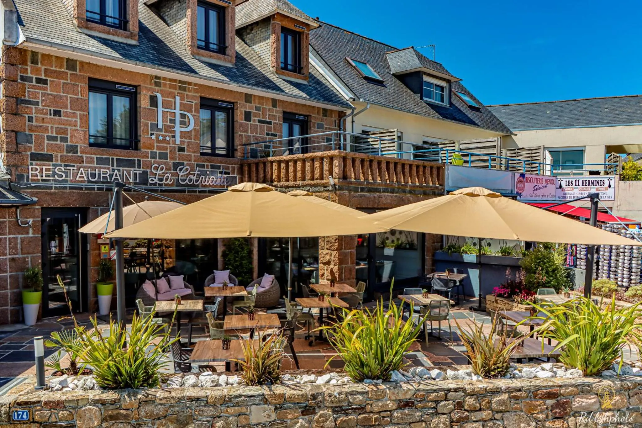 Terrasse ombragée avec tables et chaises devant un bâtiment en pierre.