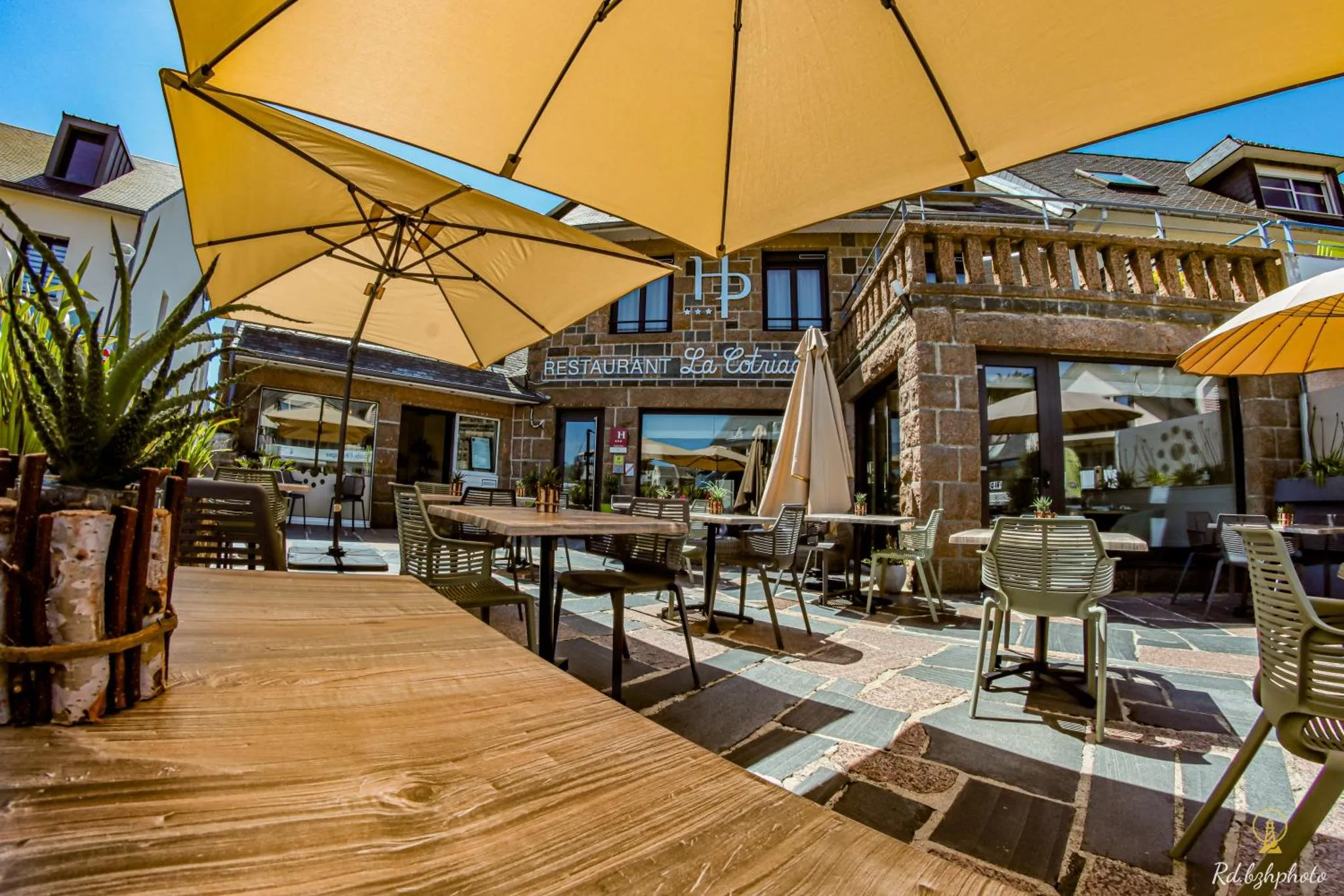 Terrasse ombragée avec tables et chaises devant un bâtiment en pierre.