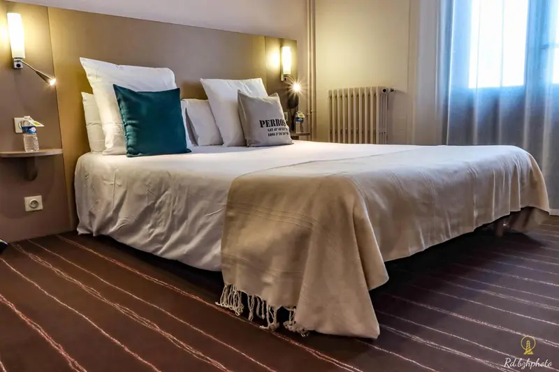 Une chambre avec un grand lit recouvert d'une couverture claire et de coussins.