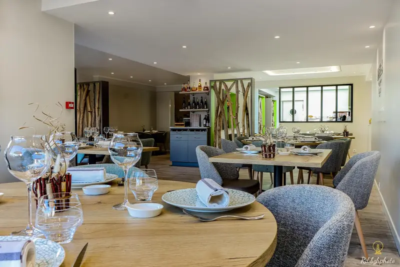 Une salle de restaurant lumineuse avec des tables dressées et un comptoir de boissons.