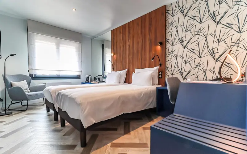 Chambre moderne avec deux lits simples et un fauteuil.