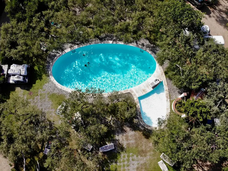 Vue aérienne d'une piscine entourée de végétation et de bâtiments.