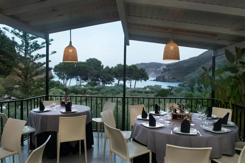 Terrasse ombragée avec tables dressées face à la mer.