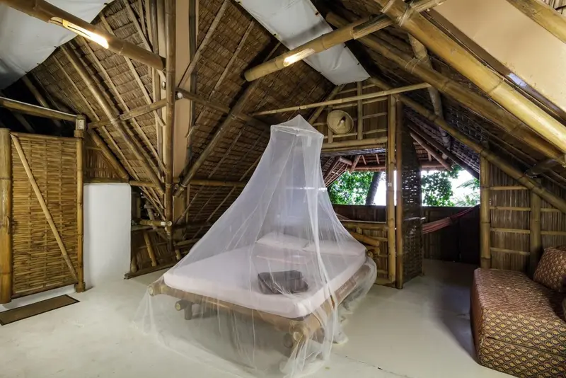 Une chambre mansardée avec un lit à baldaquin en bois et moustiquaire.