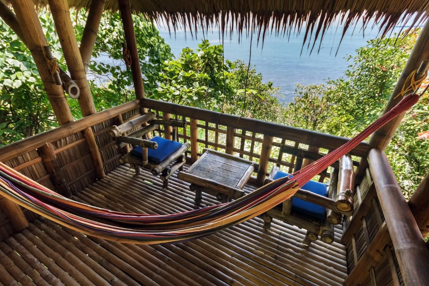 Terrasse en bois avec hamac et mobilier de détente face à la mer.