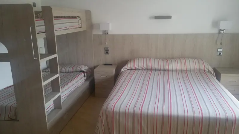 Une chambre avec un lit superposé et un lit double est aménagée avec des meubles en bois clair.