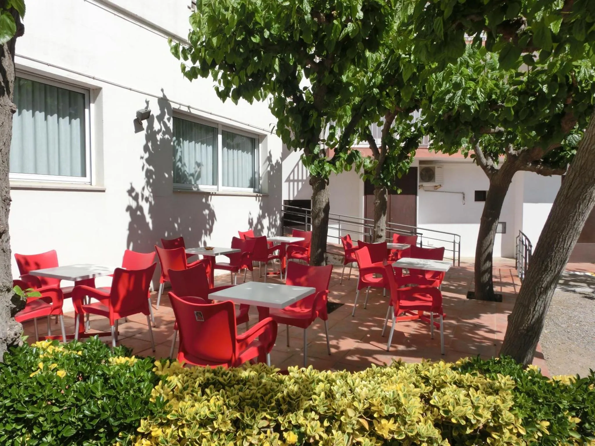Terrasse ombragée avec tables et chaises rouges.