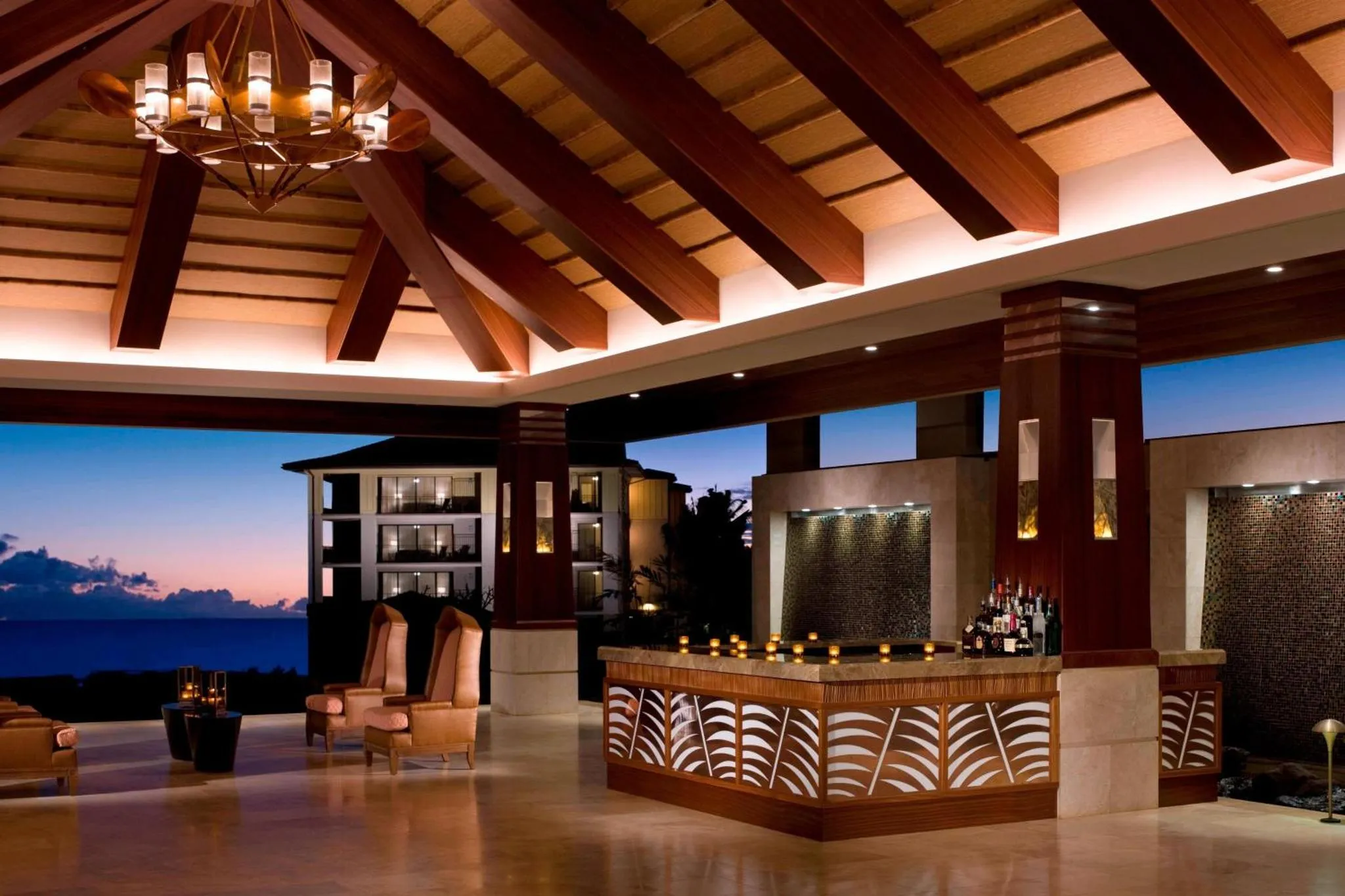 Un bar avec un comptoir en bois et des fauteuils confortables offre une vue sur la mer au crépuscule.