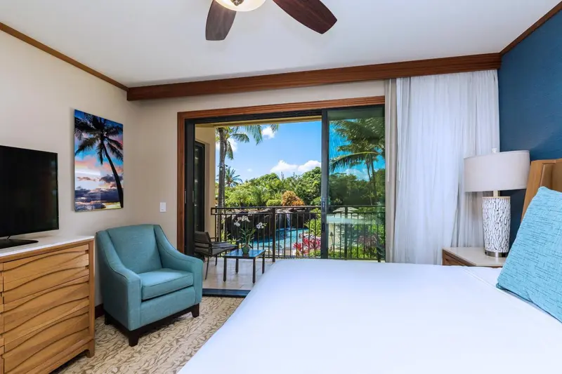 Une chambre lumineuse avec un fauteuil et une vue sur une terrasse et une piscine.