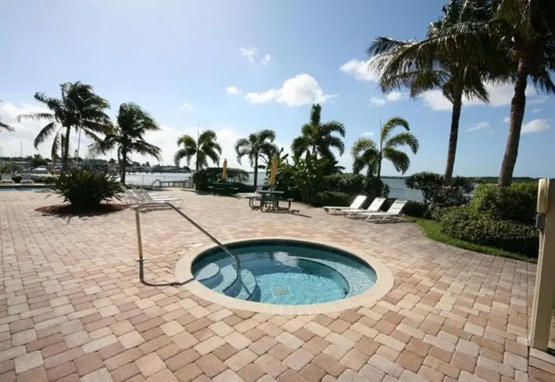 Un jacuzzi encastré dans une terrasse pavée, avec des transats et des palmiers en arrière-plan.