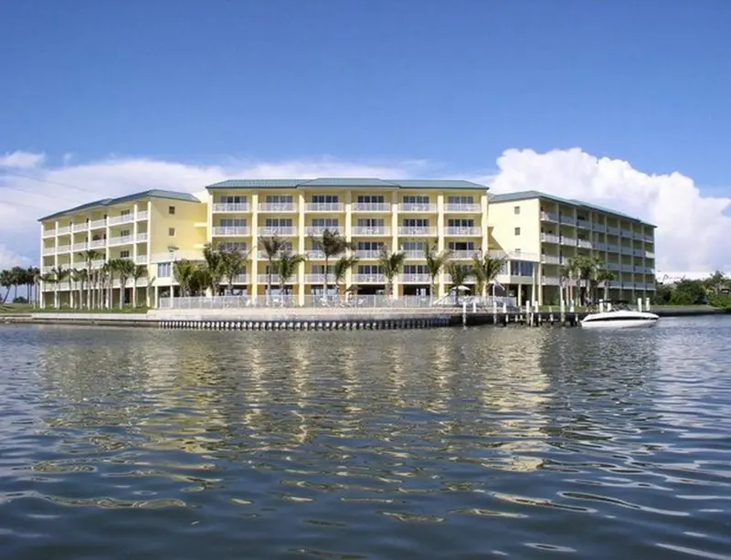 Bâtiment jaune à plusieurs étages au bord de l'eau, avec des palmiers.