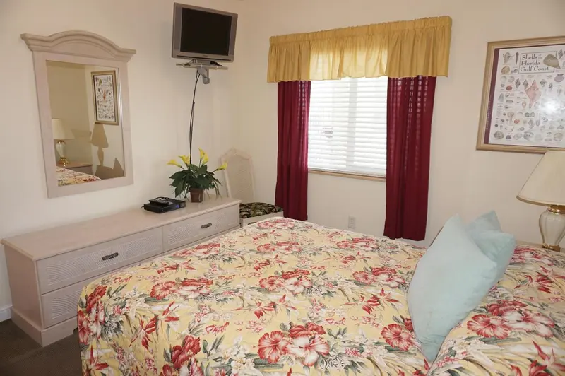 Une chambre lumineuse avec un lit recouvert d'une couette fleurie et un miroir au-dessus d'une commode.