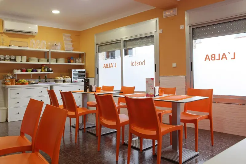 Une salle lumineuse avec des tables et des chaises orange, un buffet de petit-déjeuner et des étagères remplies de vaisselle.
