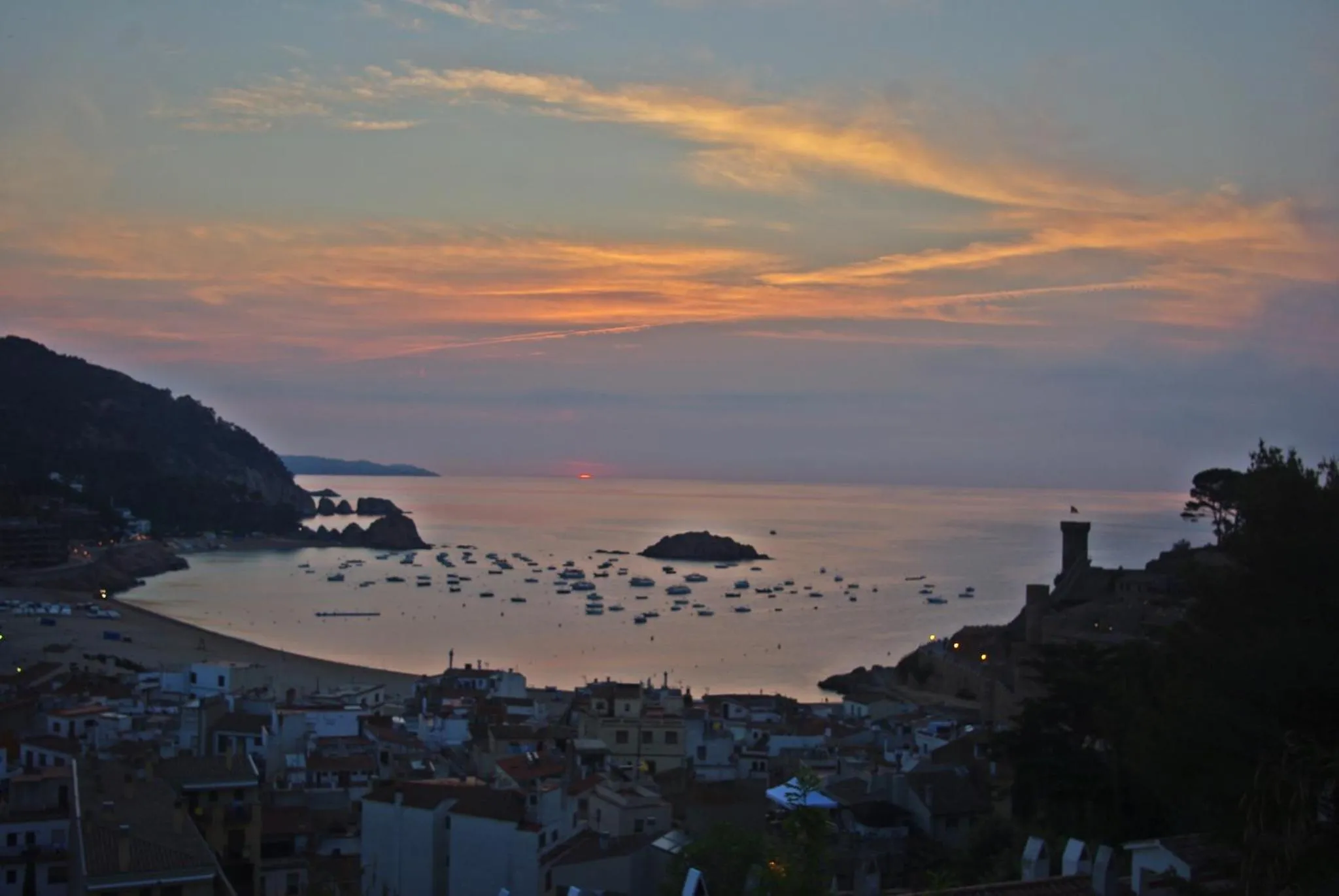Coucher de soleil sur une baie avec des bateaux amarrés et un village côtier.