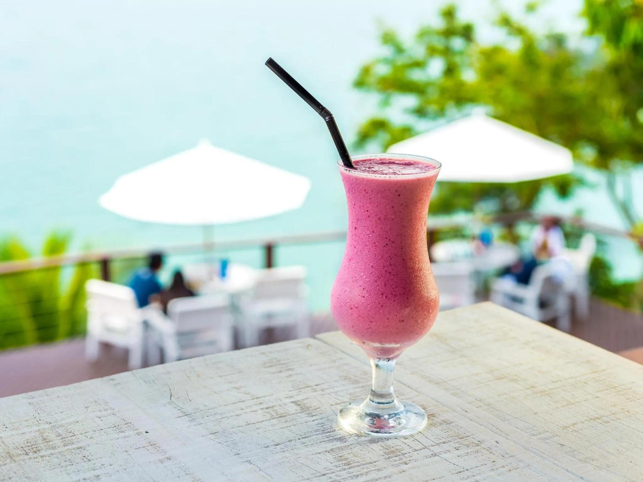 Un cocktail fruité est servi sur une terrasse ensoleillée avec vue sur la mer.