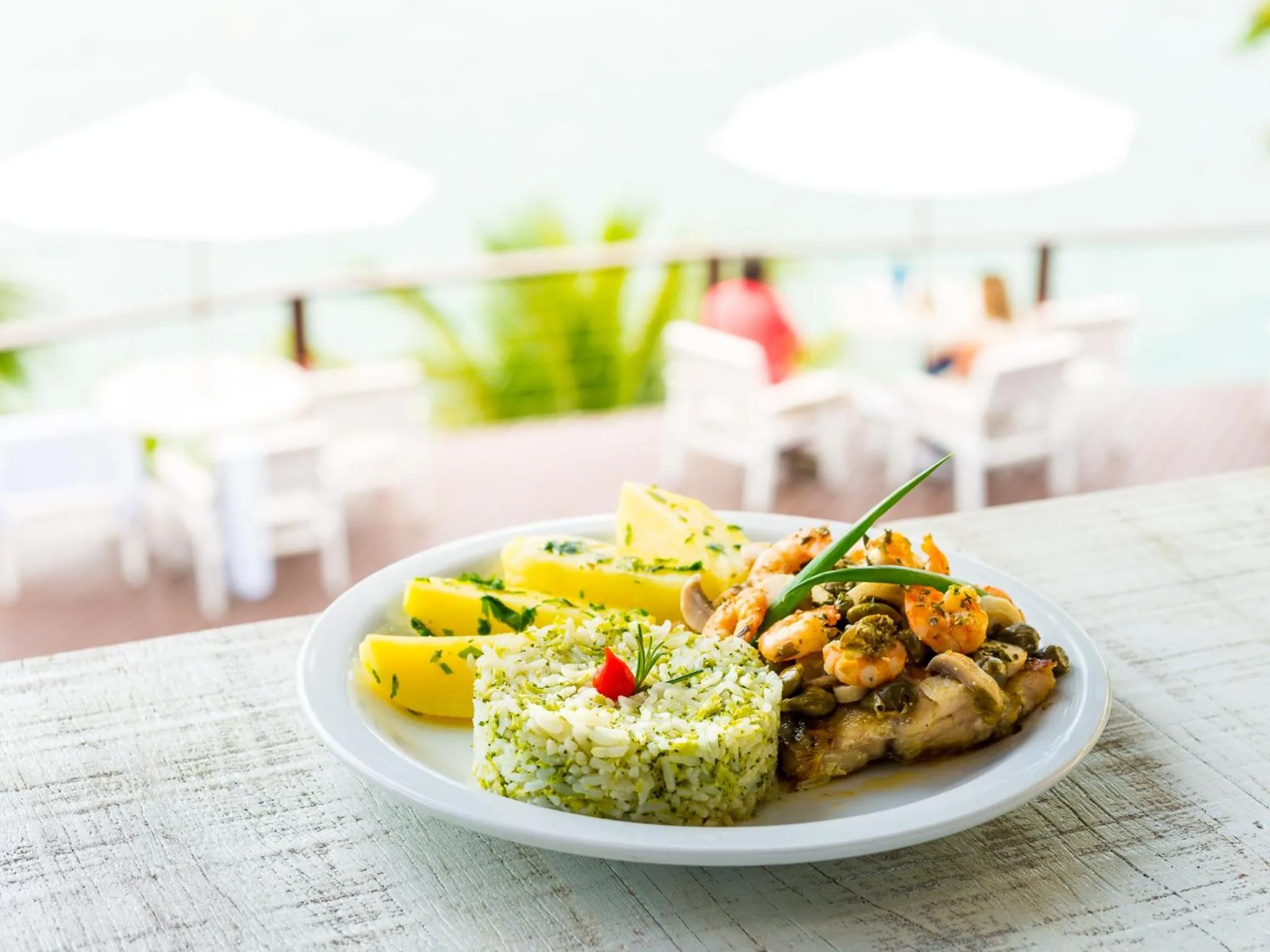 Assiette de riz et de fruits de mer sur une table en terrasse avec vue sur la mer.