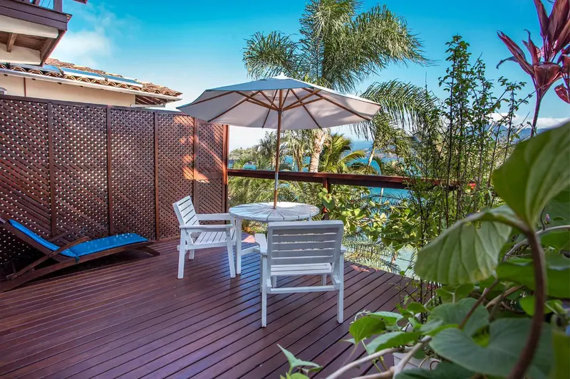 Terrasse en bois avec mobilier blanc et vue sur la végétation et la mer.