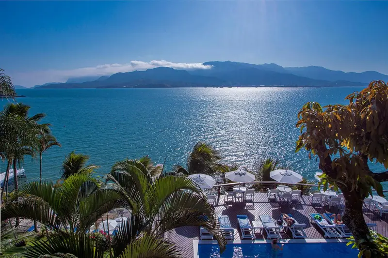 Vue panoramique sur la mer et les montagnes depuis une terrasse ensoleillée.