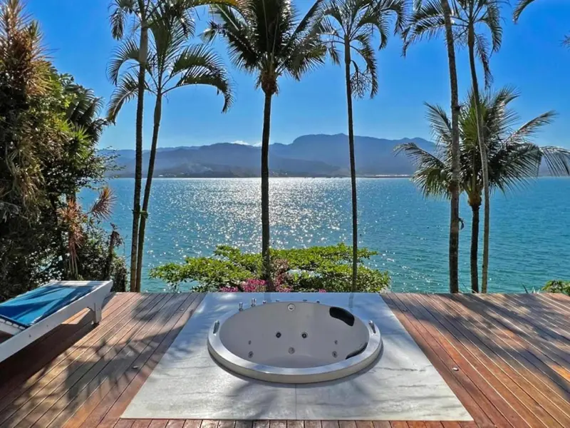 Un jacuzzi encastré dans une terrasse en bois surplombe la mer et les montagnes.