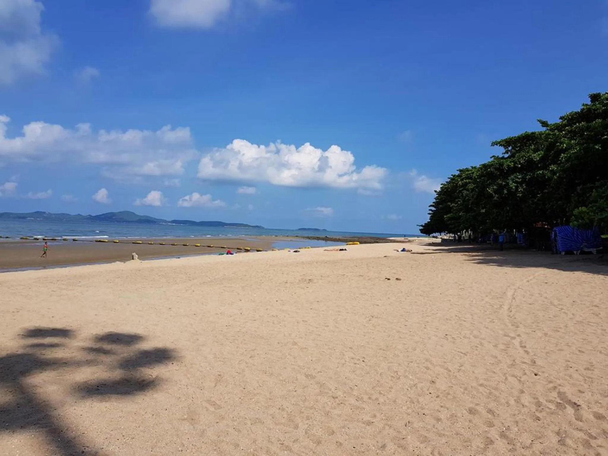 Plage de sable fin bordée d'une eau turquoise sous un ciel nuageux.