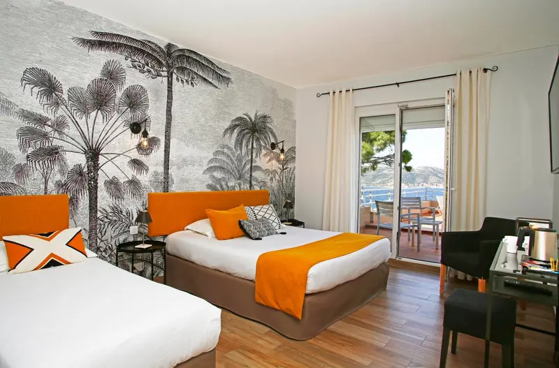 Chambre lumineuse avec lits jumeaux et vue sur la mer depuis un balcon.