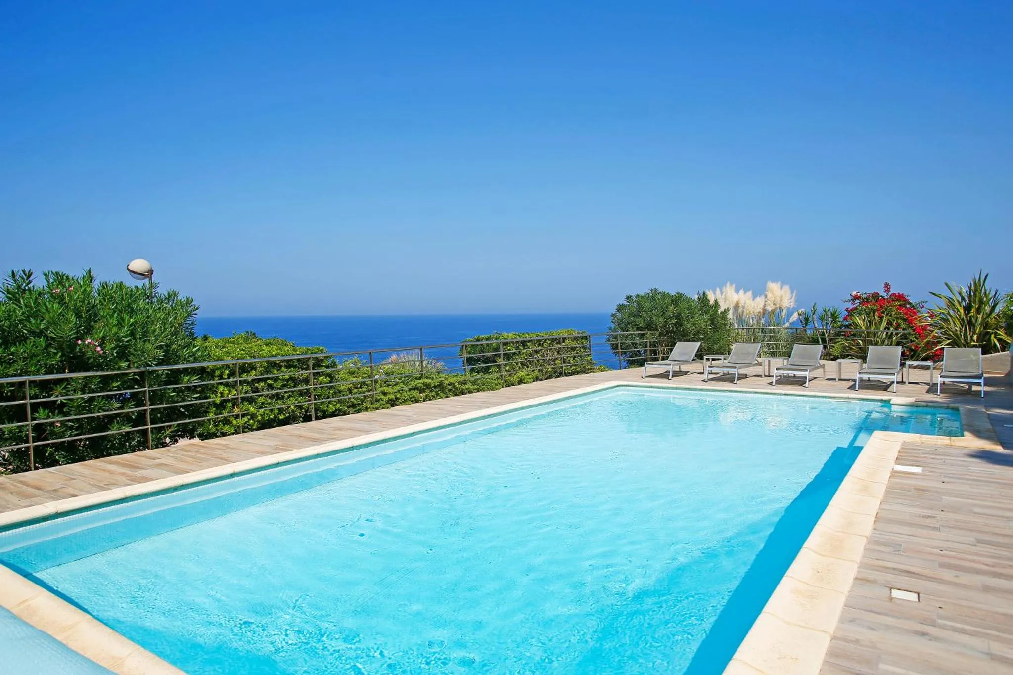 Une piscine rectangulaire avec terrasse ensoleillée et vue sur la mer.