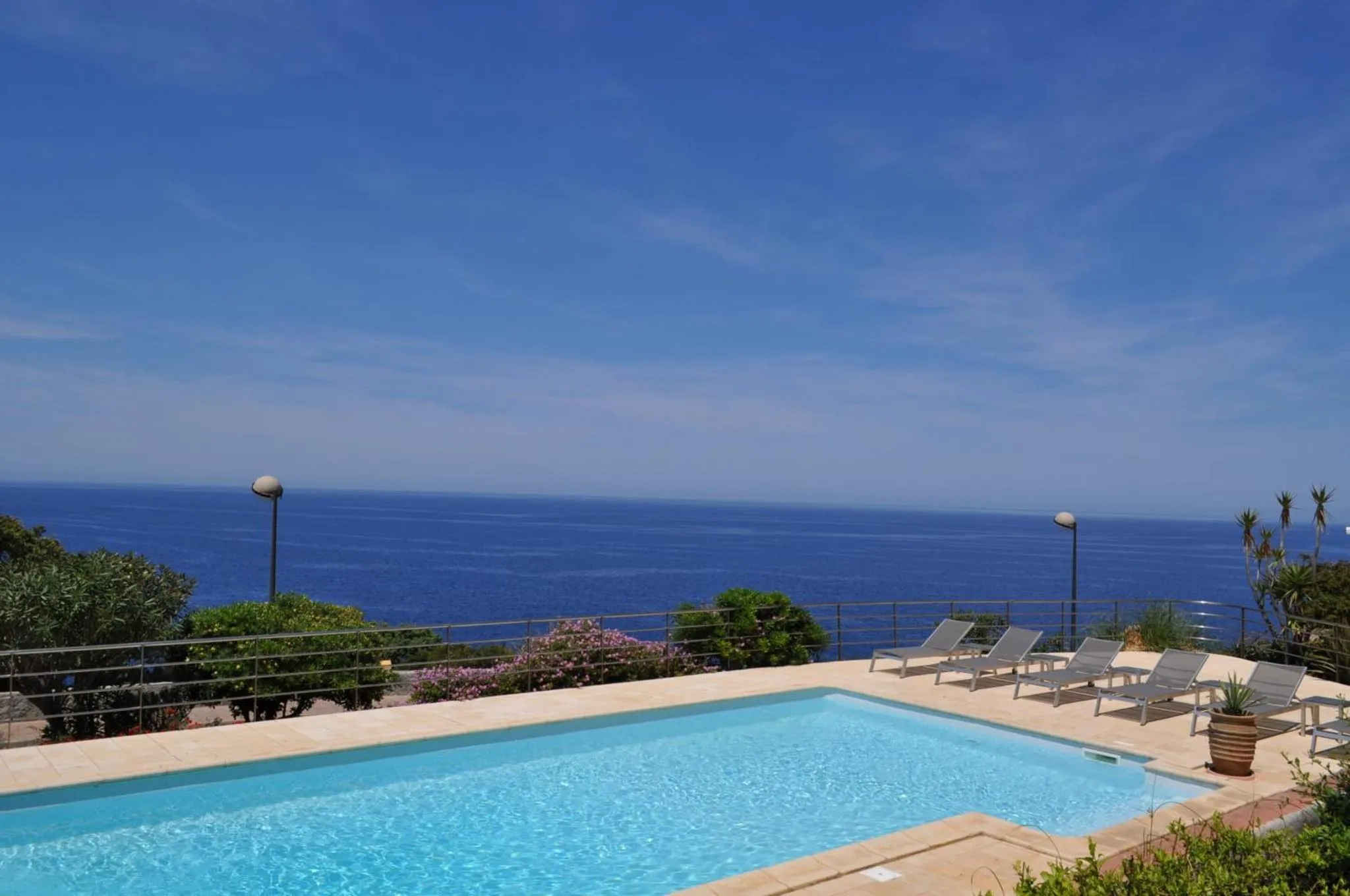 Transats alignés au bord d'une piscine face à la mer.