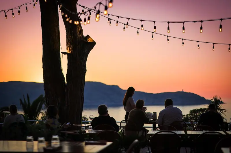 Des convives sont attablés en terrasse au coucher du soleil.