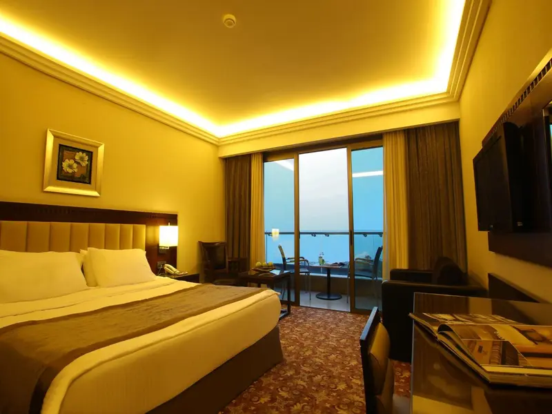 Chambre lumineuse avec un grand lit et une vue sur la mer depuis un balcon.
