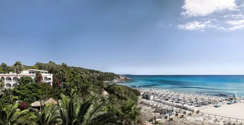 Vue aérienne d'une plage de sable fin bordée de parasols et d'une végétation luxuriante.