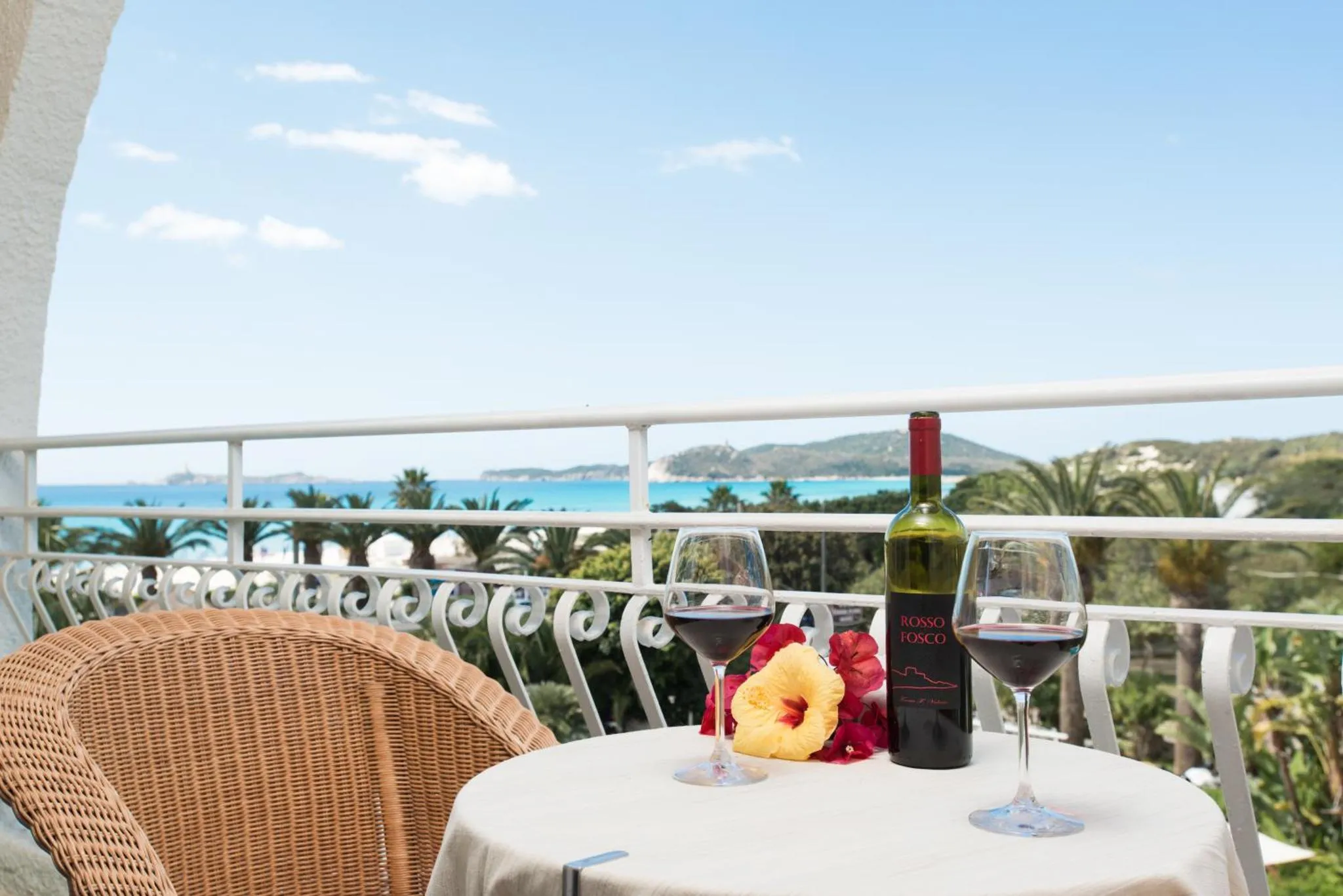 Une table avec une bouteille de vin et des verres sur un balcon avec vue sur la mer.