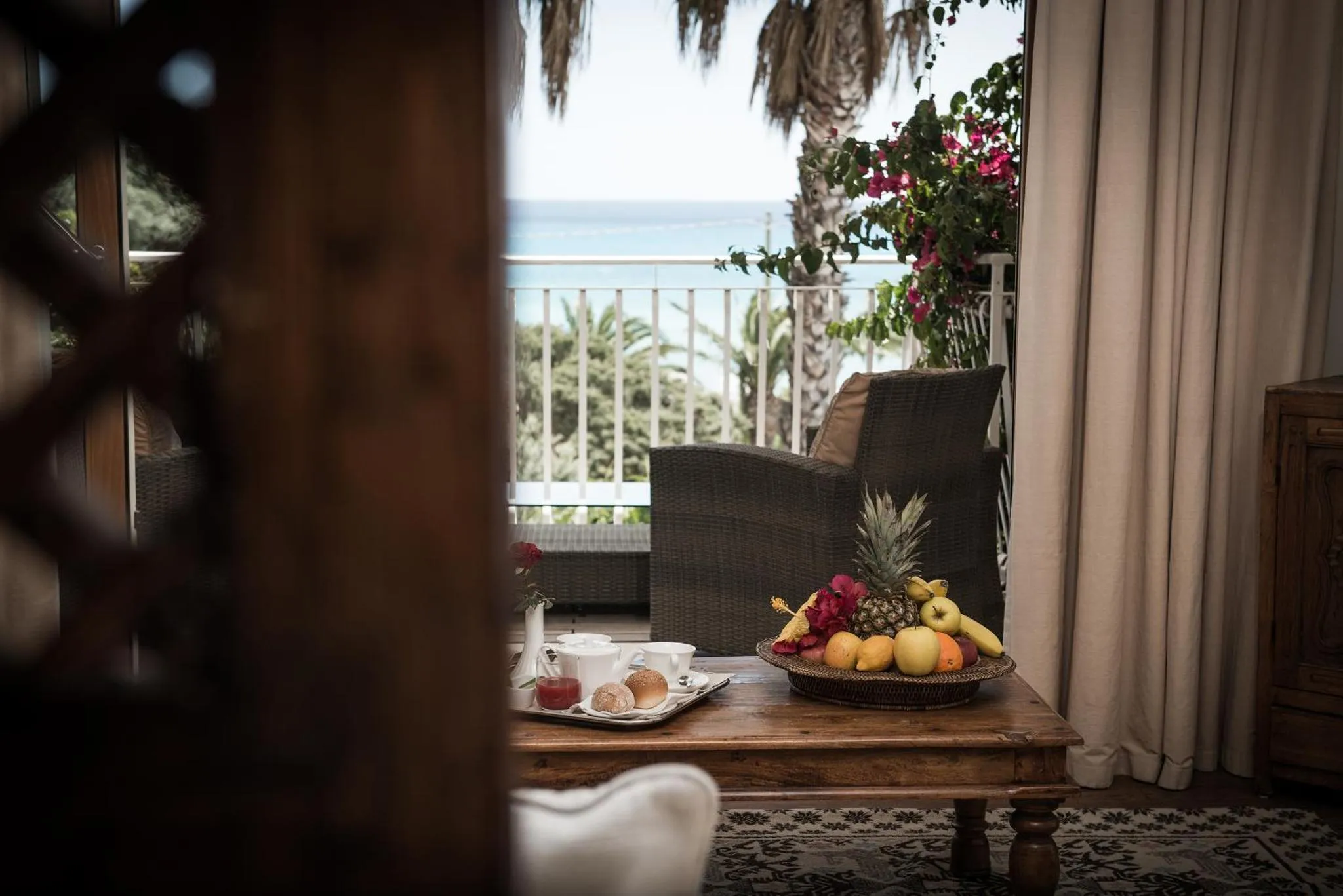 Une table basse avec un plateau de fruits et des boissons est mise en scène devant une vue sur la mer.
