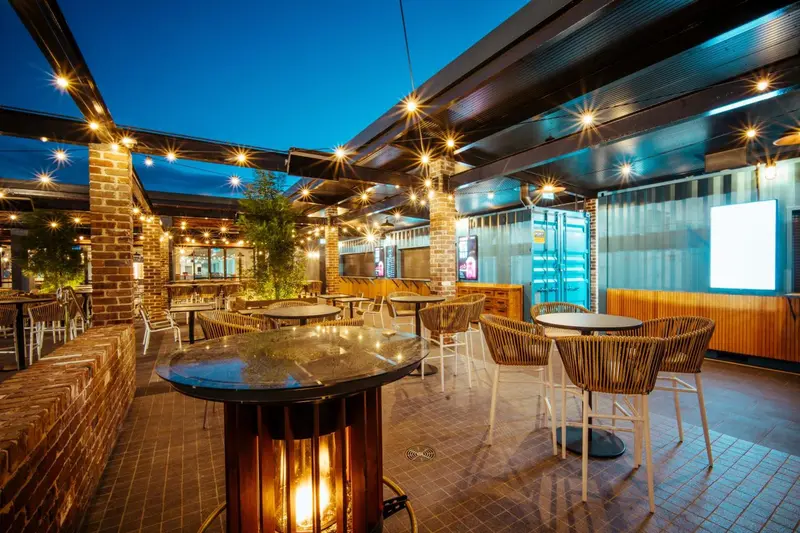 Terrasse lumineuse avec tables et chaises, éclairée par des guirlandes et des chauffages d'extérieur.