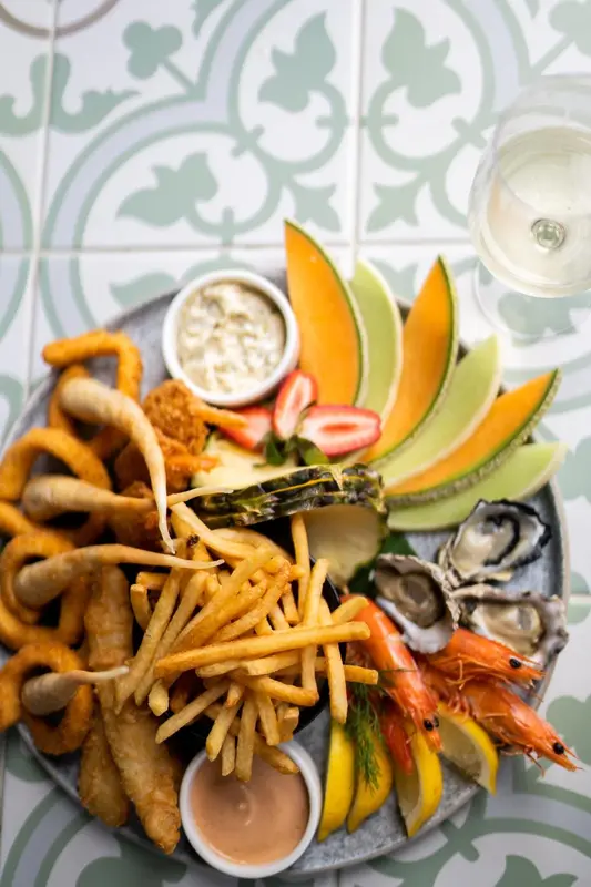 Assiette généreuse de fruits de mer et de frites présentée sur une table carrelée.