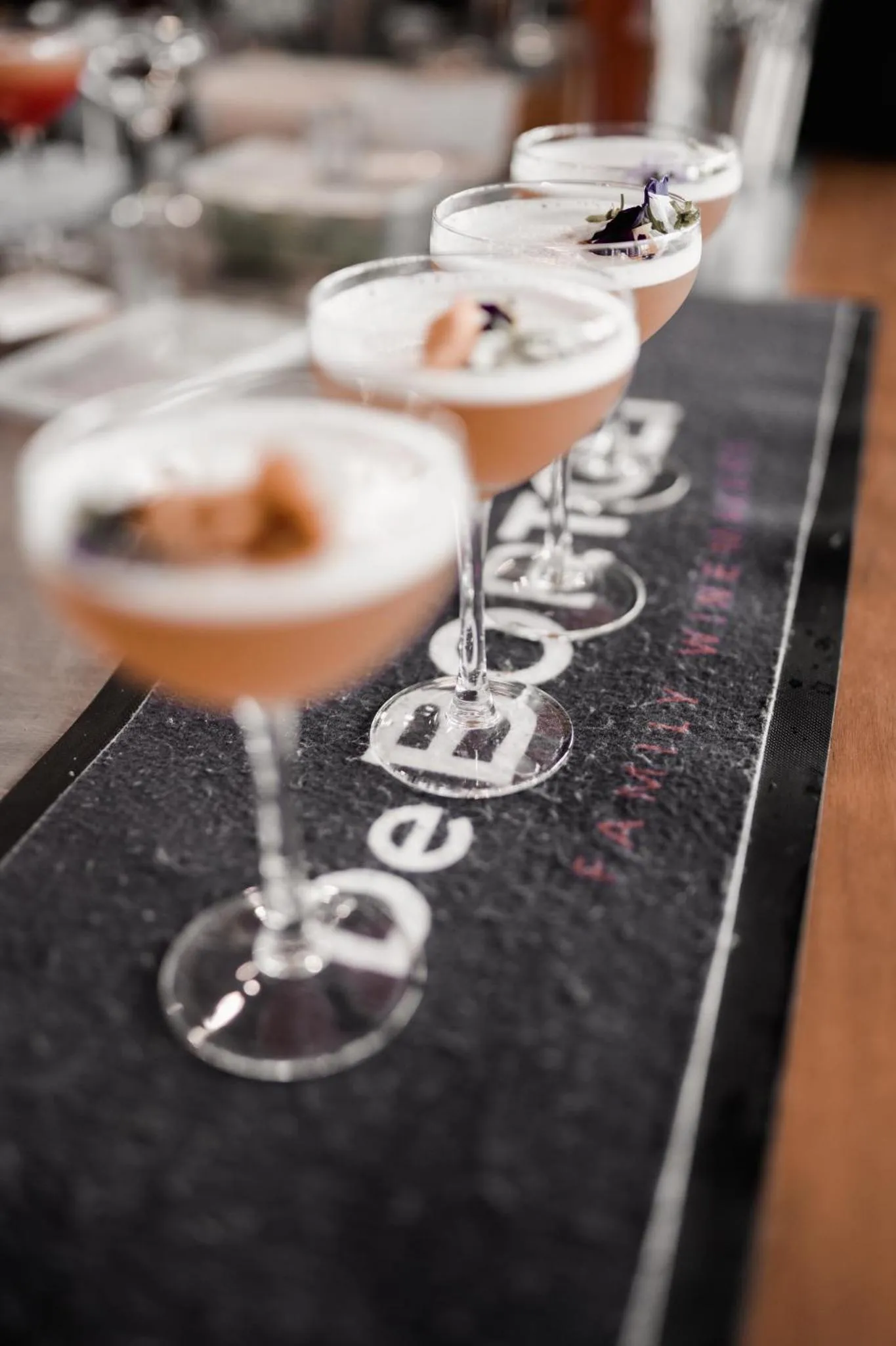 Une rangée de cocktails colorés est présentée sur un comptoir sombre.
