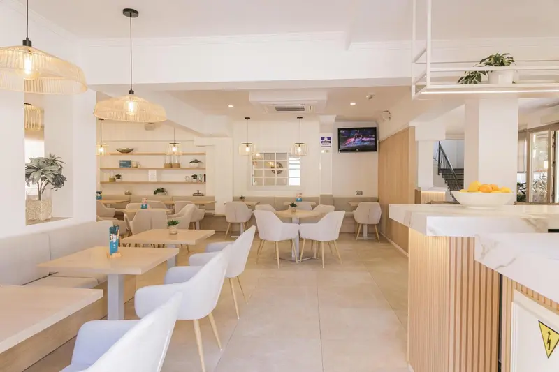 Une salle lumineuse avec des tables et des chaises claires, un comptoir et des suspensions décoratives.