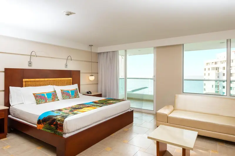 Une chambre lumineuse avec un grand lit et un coin salon donnant sur la mer.