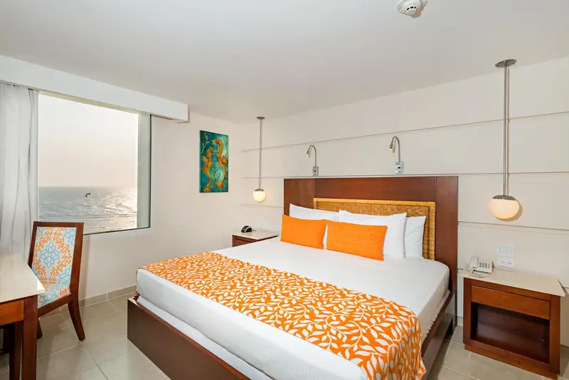 Chambre lumineuse avec un lit recouvert d'une courtepointe orange et une vue sur la mer.