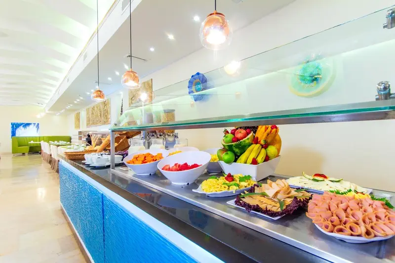 Un buffet propose une variété de fruits, de pâtisseries et de charcuteries dans une salle lumineuse.