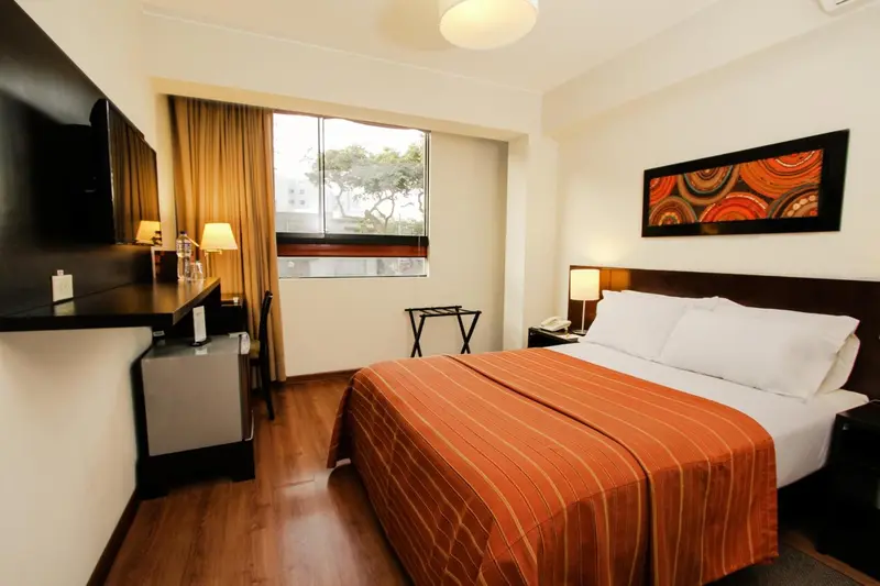 Une chambre d'hôtel lumineuse avec un grand lit recouvert d'une courtepointe orange.