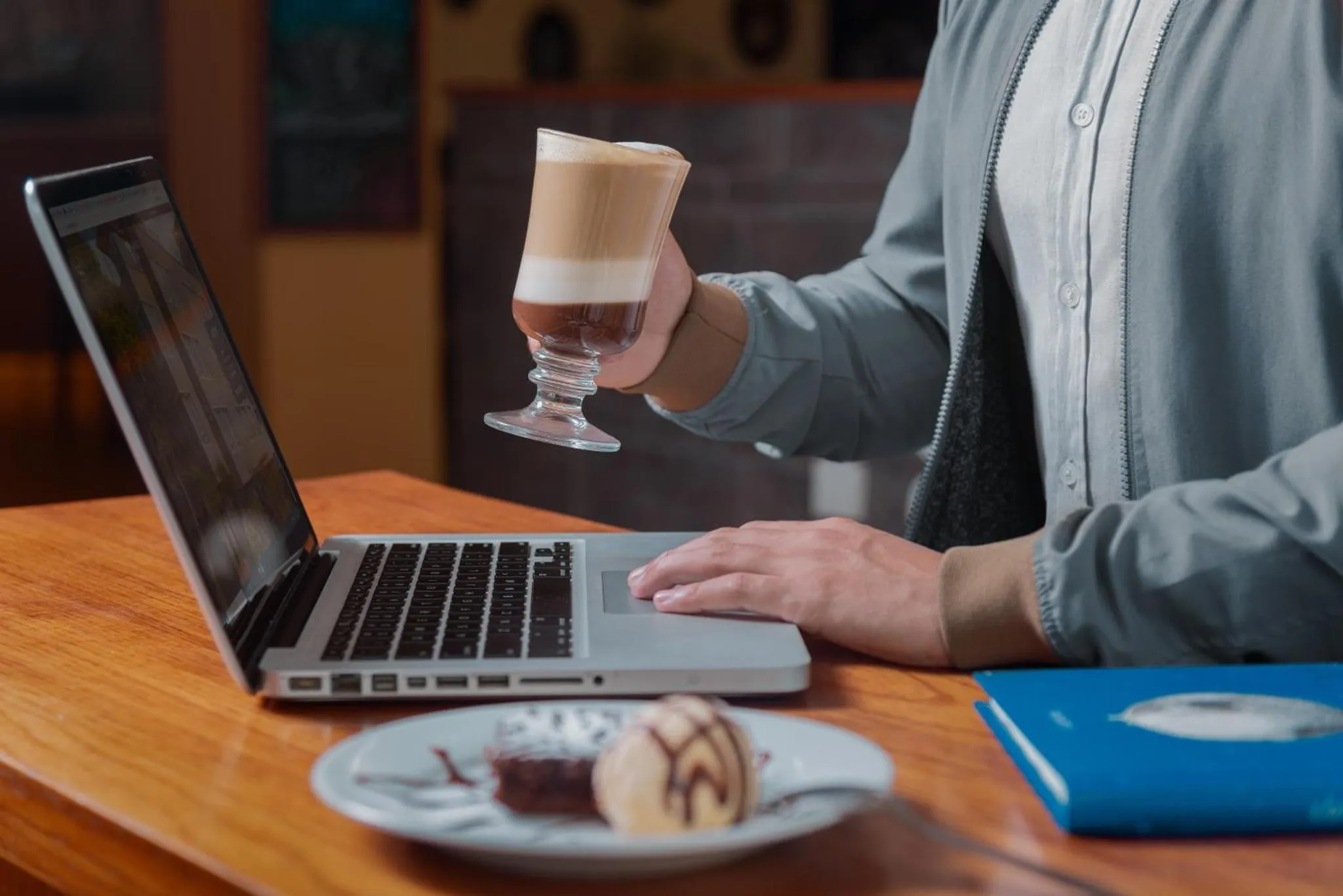 Une personne travaille sur un ordinateur portable devant une table avec une boisson et une pâtisserie.