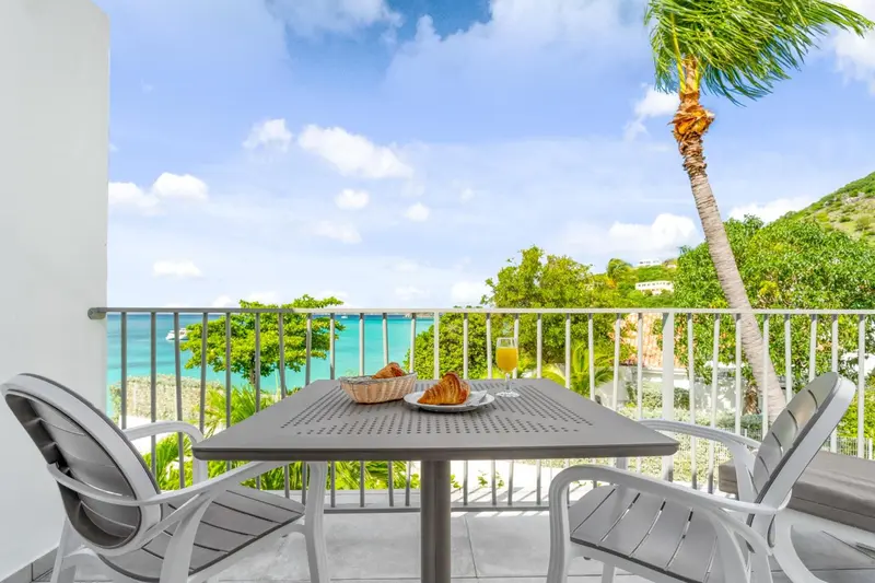 Une table avec un petit-déjeuner est mise en scène sur une terrasse ensoleillée avec vue sur la mer.