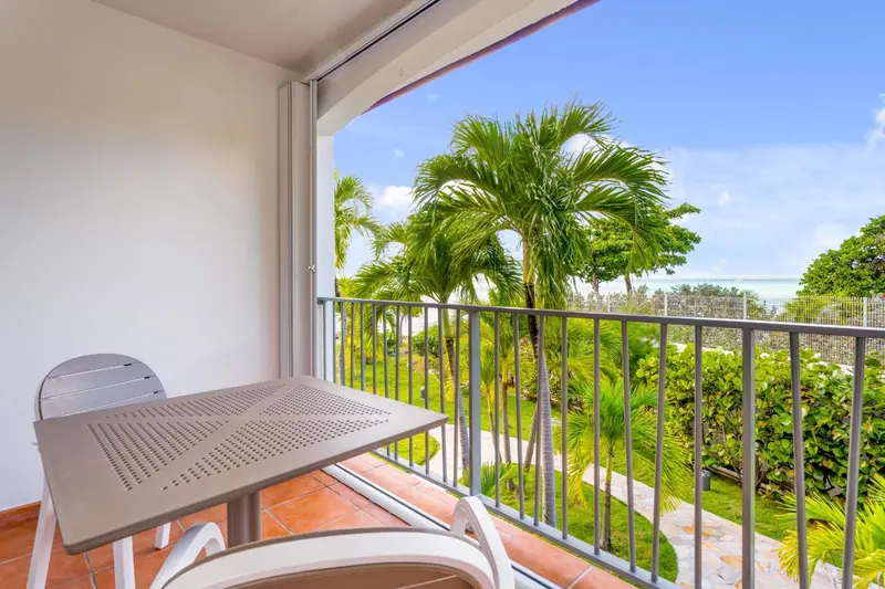 Une table et des chaises blanches sur une terrasse carrelée donnant sur une végétation luxuriante.