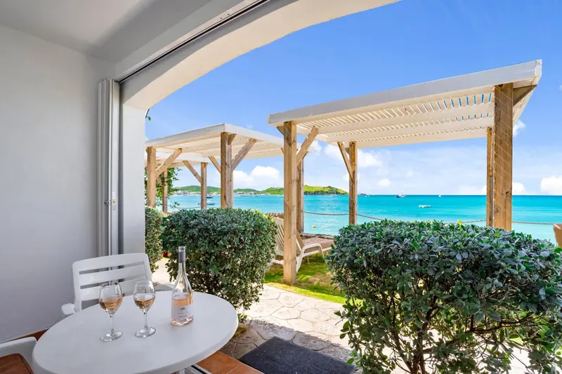 Une table ronde avec des verres de vin est placée devant une terrasse ombragée donnant sur la mer.