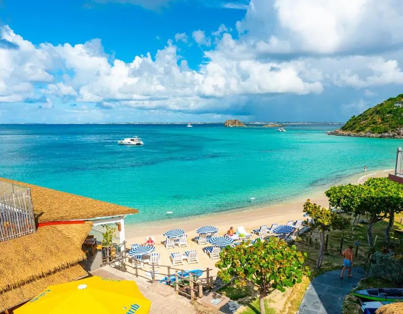 Vue aérienne d'une plage de sable blanc bordée de transats bleus et d'une mer turquoise.