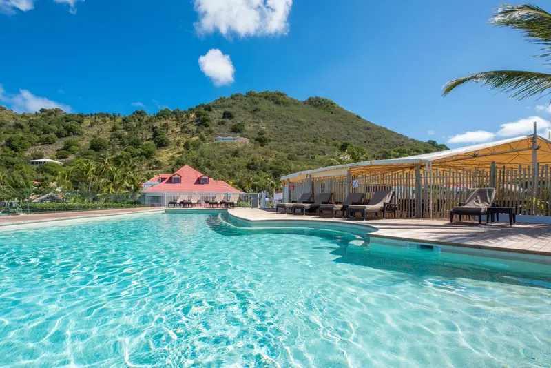Une piscine turquoise bordée de chaises longues sous un abri en bois.