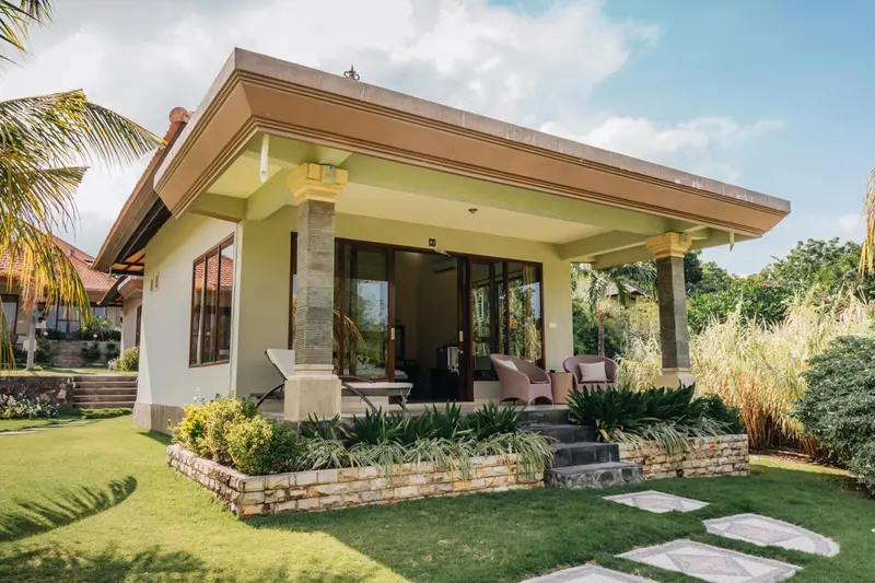 Façade d'une maison basse avec une terrasse ombragée et un jardin soigné.