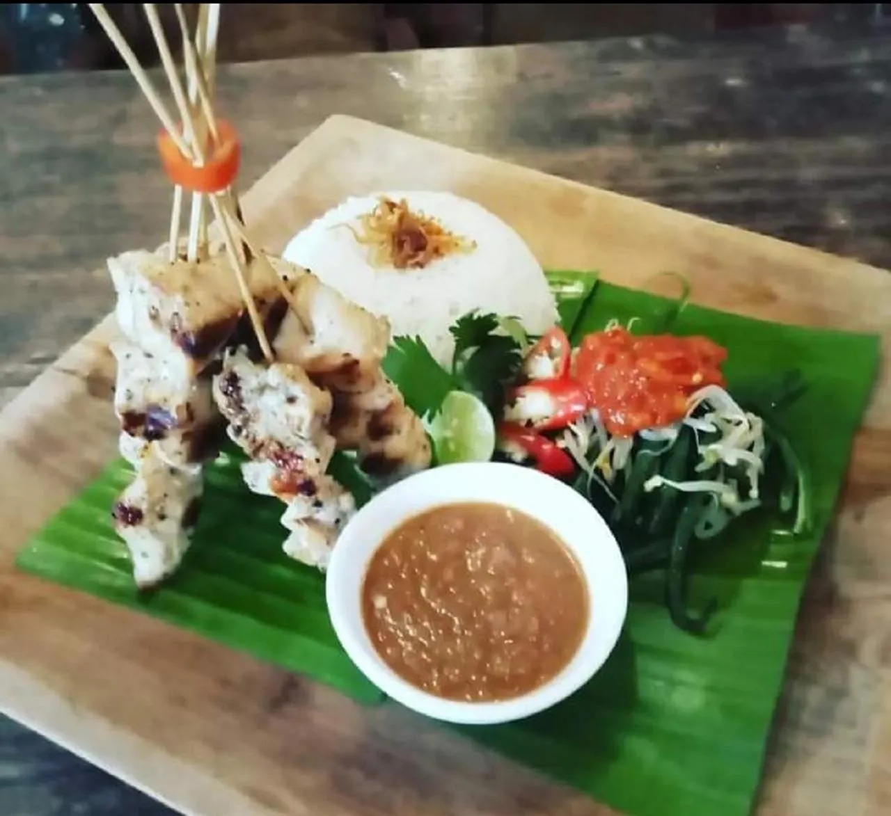 Assiette de riz accompagnée de brochettes de poulet, de légumes et d'une sauce.